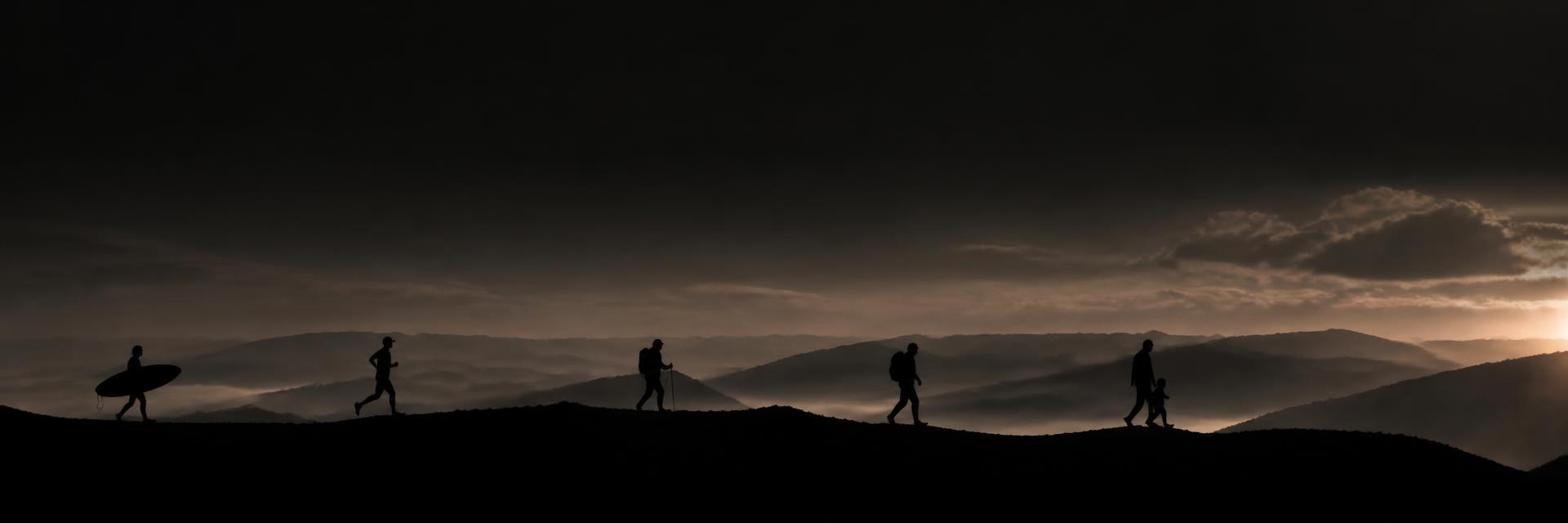 Silhouettes of a surfer, runner, hiker, backpacker and a parent with a child spaced along a mountain ridge at dusk